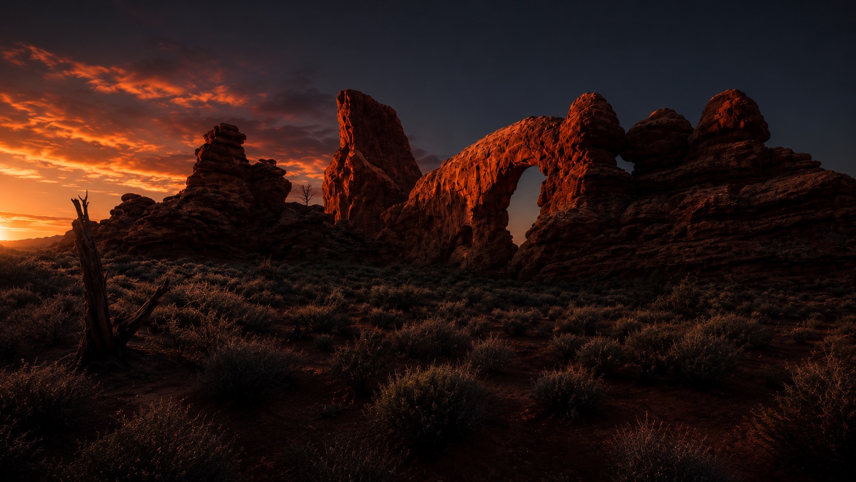 Red rock arch and sandstone formations glowing at sunset under a fiery desert sky