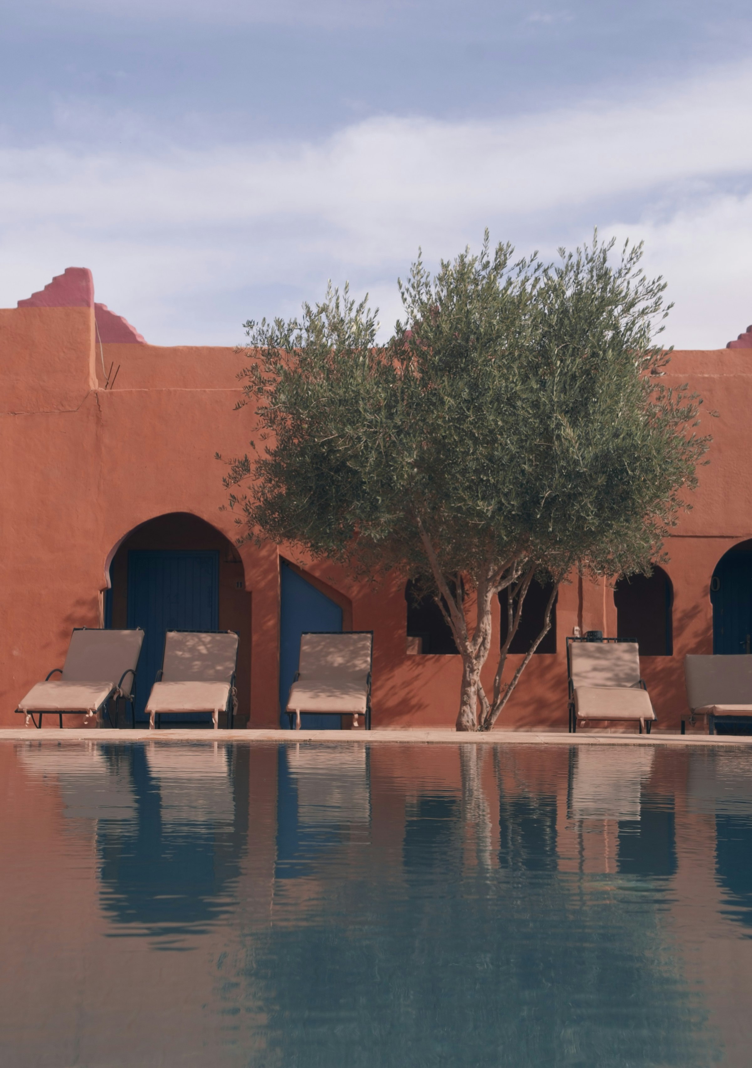 Rust-walled resort courtyard with loungers beneath an olive tree